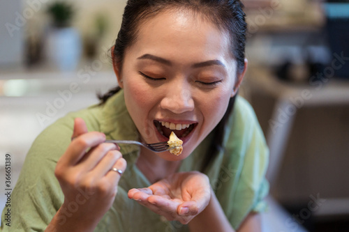 Happy young pretty Asian woman eating delicious chocolate tart on bed