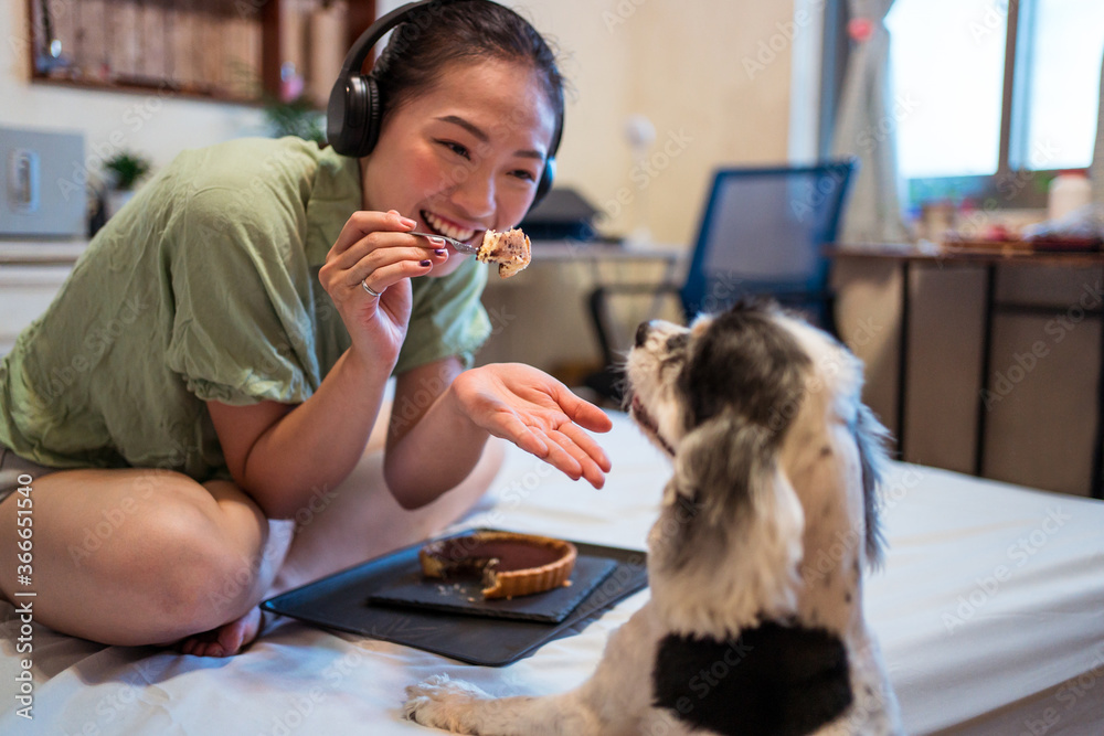 Young pretty Asian woman eating delicious chocolate tart on bed
