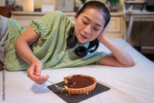 Obraz na płótnie Young pretty Asian woman eating delicious chocolate tart lying on bed w salonie