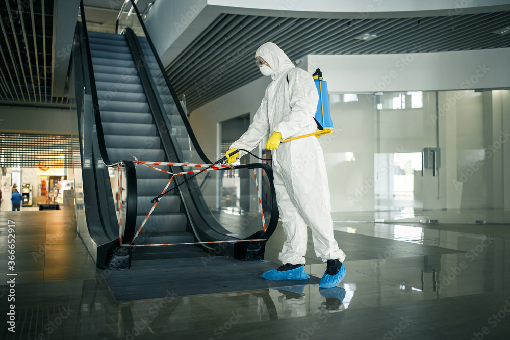 Sanitizing worker disinfects the escalator with a spray at the empty shopping mall to prevent the covid-19 spread in public places. Healthcare, clean, isolation and quarantine concept. Sanitizing worker disinfects the escalator with a spray at the empty shopping mall to prevent the covid-19 spread in public places. Healthcare, clean, isolation and quarantine concept.