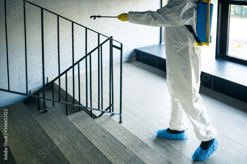 Sanitizing worker cleaning up the staircase at the shopping mall with an antiseptic to prevent covid-19 spread. A man in a disinfection suit sprays stairs. Healthcare, quarantine and hygiene concept. © Konstantin Zibert