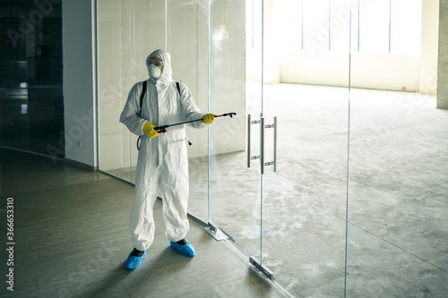 Sanitary worker sprays an empty business center with antiseptical liquid to prevent covid-19 spread. A man wearing disinfection suit cleaning up the shopping mall. Nobody, health, isolated concept. © Konstantin Zibert