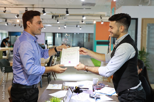 two caucasian businessmen shaking hands while holding success business certificate with happy and smiling face