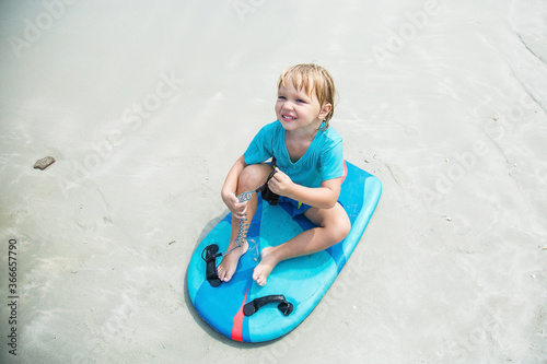 baby sits on a bodyboard on the sand by the sea