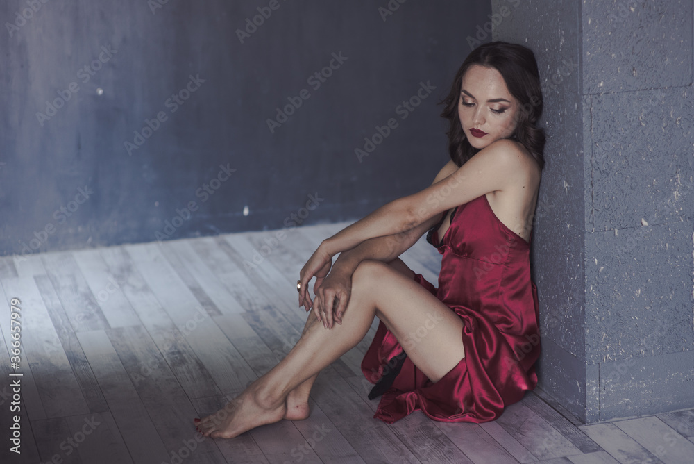 Naklejka premium Hot young gir sits in black room in red sleep dress. Soft focus.