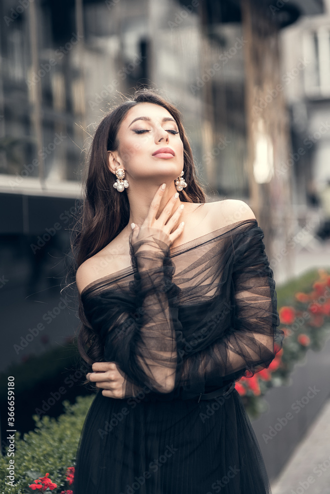 Girl in sexy black dress poses on a street. Soft selective focus Girl in sexy black dress poses on a street. Soft selective focus