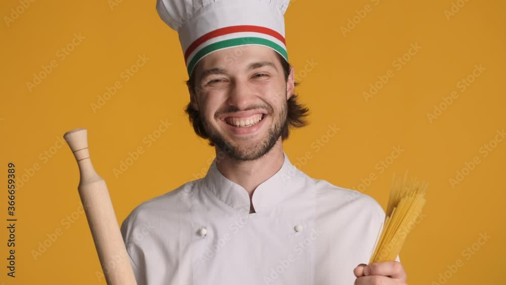 Portrait of handsome italian chef in uniform holding rolling pin and macaroni happily smiling on camera over colorful background Portrait of handsome italian chef in uniform holding rolling pin and macaroni happily smiling on camera over colorful background