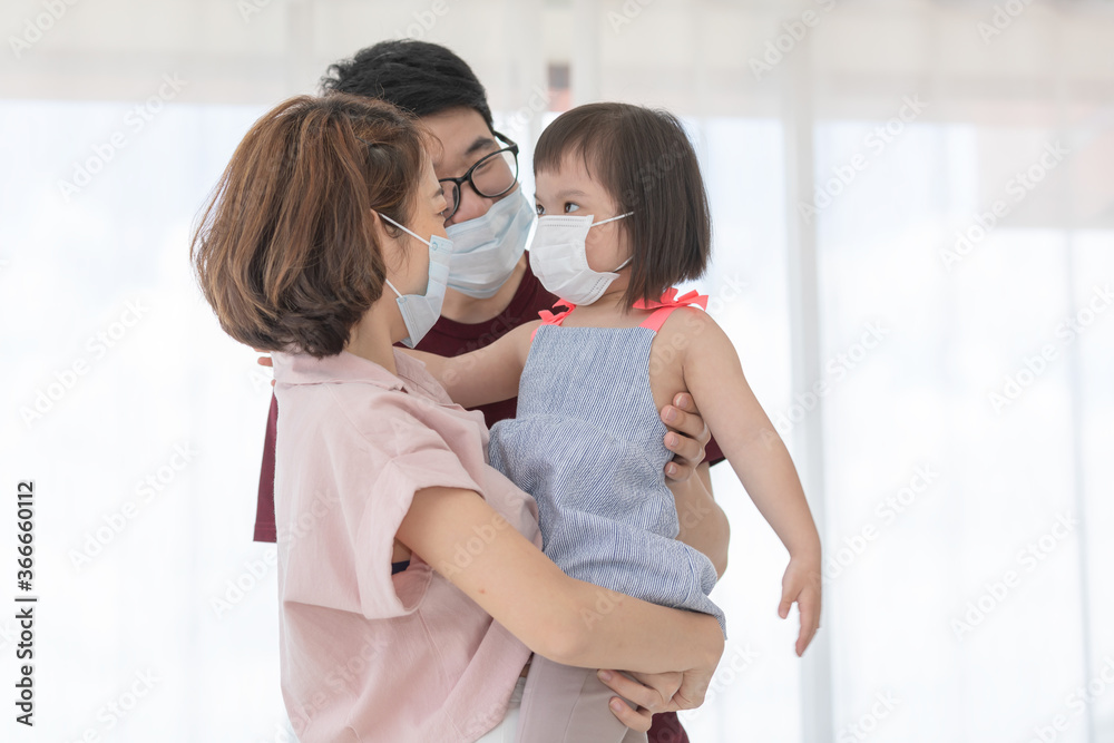 Asia Family in medical masks on the face looks at the camera while standing in the living room at home to prevent PM2.5 dust, smog, air pollution and COVID-19. Healthcare concept.