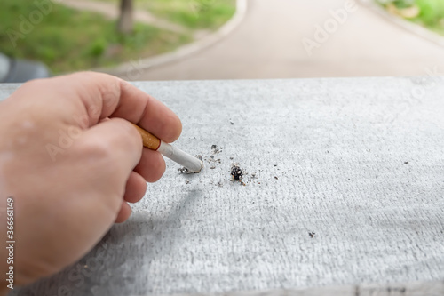 the hand of a Smoking person puts out a cigarette butt on the window sill of a home window with a view of the street