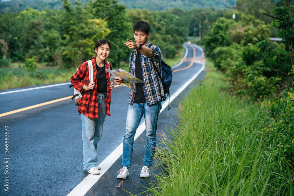 Male and female tourists look at the map on the road. Male and female tourists look at the map on the road.