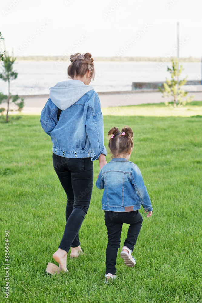 Lifestyle portrait of mom and daughter happy on the outside. Family time together. Modern family look denim. Mother's Day, love family, parenthood, childhood concept. Back view