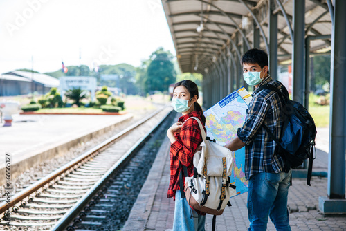 Both male and female tourists look at the map beside the railway.