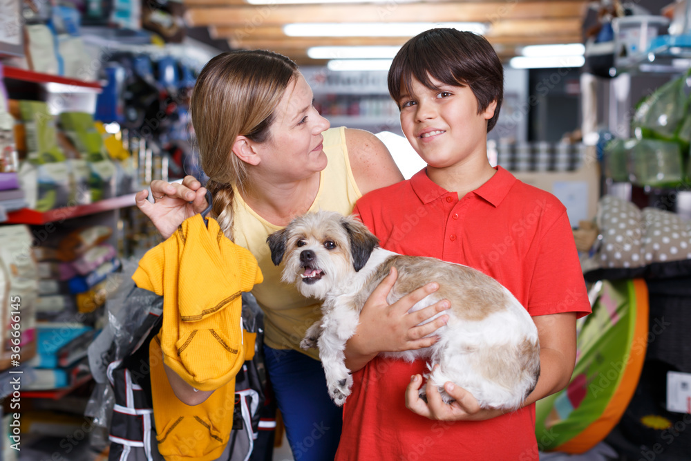 Cheerful woman with son buying new dog clothes in store for their pup