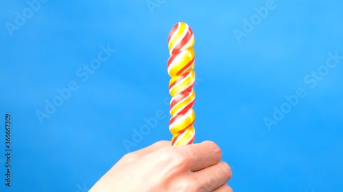 Close up of female hands. In a female hand a candy lollipop, on the other hand, a woman imitates masturbation. Blue simple background.