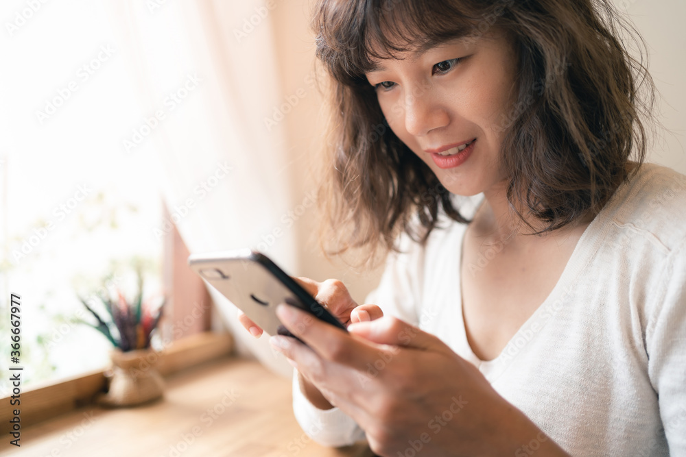 Close up of young Asian woman using smartphone chatting and searching information with blurry smiley face background. Technology business and social distancing concept Close up of young Asian woman using smartphone chatting and searching information with blurry smiley face background. Technology business and social distancing concept