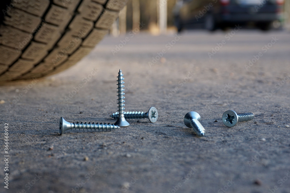 Ταπετσαρία Several screws lie on the road, one stands upright in front of the car wheel