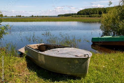 Boats stand  leaning out of the water onto the riverbank overgrown with green grass.