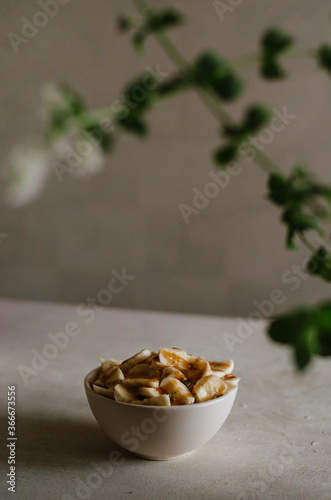 Pretty small ivory bowl with sliced banana on table in the kitchen with mint leaves decoration. Tasty and healthy vegetarian food isolated close up