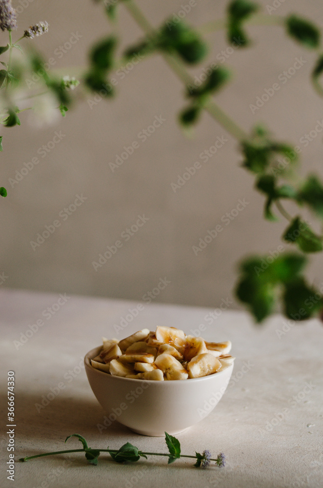 Pretty small ivory bowl with sliced banana on table in the kitchen with mint leaves decoration. Tasty and healthy vegetarian food isolated close up Pretty small ivory bowl with sliced banana on table in the kitchen with mint leaves decoration. Tasty and healthy vegetarian food isolated close up