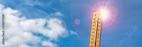Thermometer against blue sunny sky. Hot summer weather concept. photo