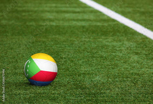 Comoros flag on ball at soccer field background. National football theme on green grass. Sports competition concept.
