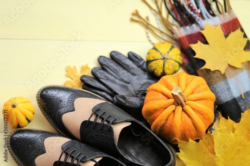 Autumn fashion accessories and shoes. Leather shoes and gloves, a scarf, maple yellow leaves and pumpkins on a yellow board wooden background. copy space.Fall fashion.Autumn discounts and sales  photo