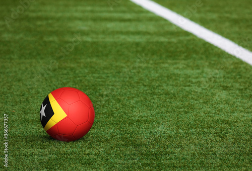 East Timor flag on ball at soccer field background. National football theme on green grass. Sports competition concept.