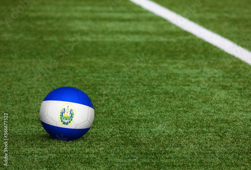 El Salvador flag on ball at soccer field background. National football theme on green grass. Sports competition concept. © sezerozger