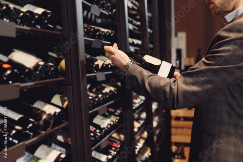 Bartender sommelier takes bottle of red wine from counter of restaurant drinks store