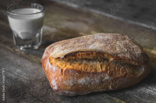 loaf of bread and glass with milk on wooden table