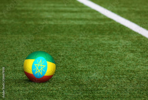 Ethiopia flag on ball at soccer field background. National football theme on green grass. Sports competition concept.