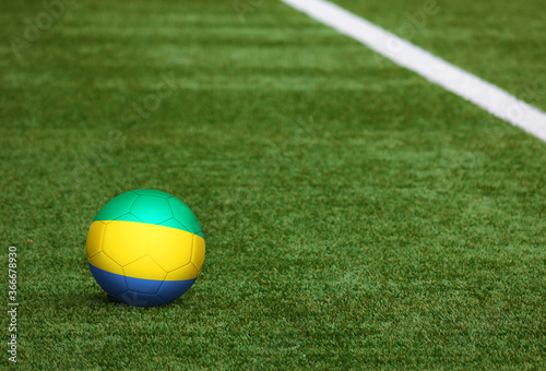 Gabon flag on ball at soccer field background. National football theme on green grass. Sports competition concept. photo