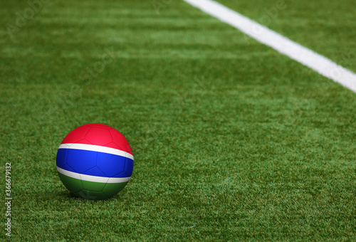 Gambia flag on ball at soccer field background. National football theme on green grass. Sports competition concept.