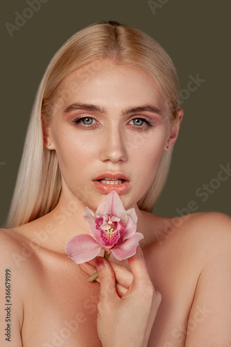 Sensual woman portrait. Organic skincare. Blonde lady with natural makeup holding orchid flower isolated on brown.