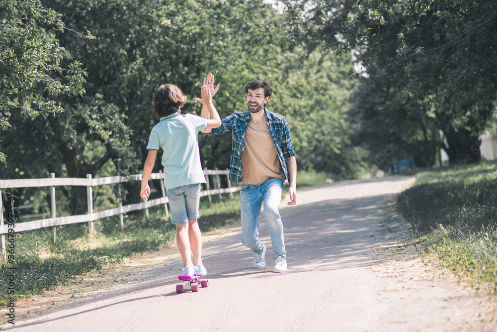 Dark-haired boy standing on a skateboard and giving high five to his dad