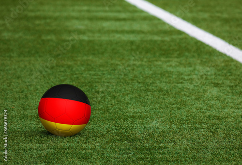 Germany flag on ball at soccer field background. National football theme on green grass. Sports competition concept.