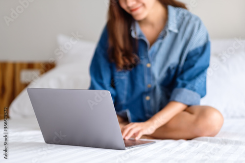 A beautiful asian woman using and working on laptop computer while sitting on a white cozy bed at home