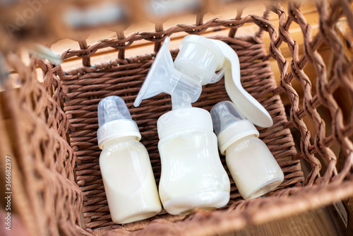 Breast pump and bottle with breast milk for baby in straw basket. Maternity and baby care concept. Top view.