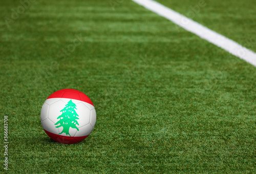 Lebanon flag on ball at soccer field background. National football theme on green grass. Sports competition concept.
