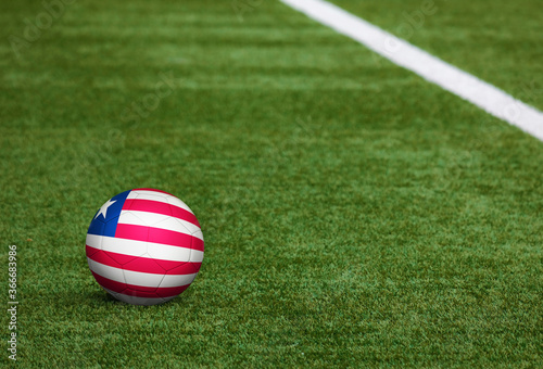 Liberia flag on ball at soccer field background. National football theme on green grass. Sports competition concept.