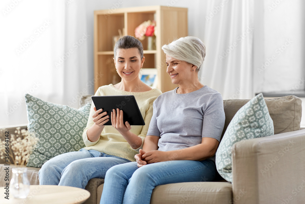 family, generation and technology concept - happy smiling senior mother and adult daughter with tablet pc computer at home family, generation and technology concept - happy smiling senior mother and adult daughter with tablet pc computer at home