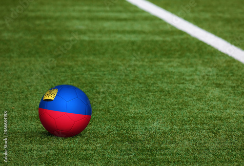 Liechtenstein flag on ball at soccer field background. National football theme on green grass. Sports competition concept.