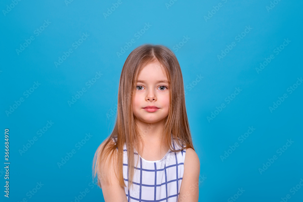 Close up shot of a little serious girl with long blonde hair against blue background with copy space in studio Close up shot of a little serious girl with long blonde hair against blue background with copy space in studio