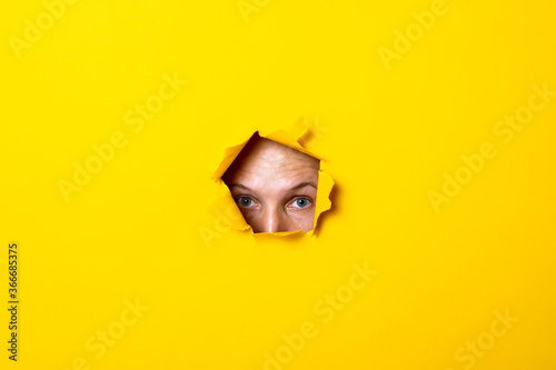 Young man looking with his eyes into the hole of torn yellow background. © Alex