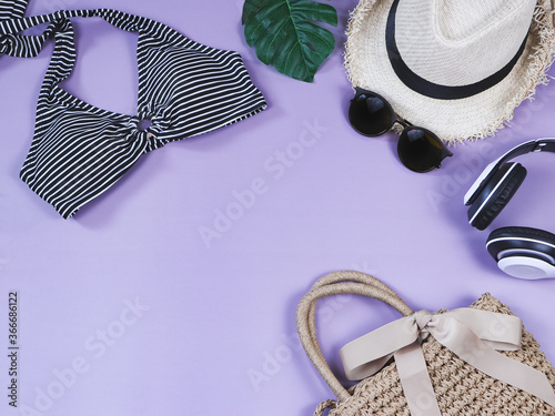 Travel and summer holiday concept, top view of black and white stripe pattern bikini swimsuit and women's vacation accessories items on purple background