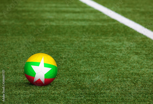 Myanmar flag on ball at soccer field background. National football theme on green grass. Sports competition concept.