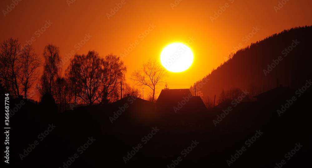 Spring sunset in the village. A solar disk hung over the horizon.