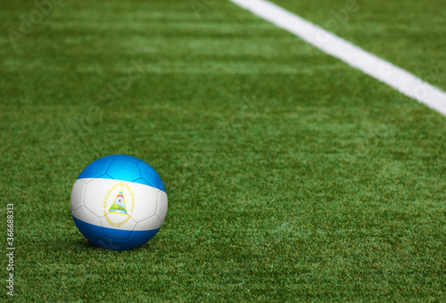Nicaragua flag on ball at soccer field background. National football theme on green grass. Sports competition concept.