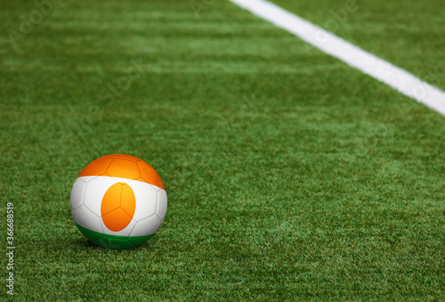 Niger flag on ball at soccer field background. National football theme on green grass. Sports competition concept.