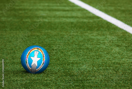 Northern Mariana Islands flag on ball at soccer field background. National football theme on green grass. Sports competition concept.